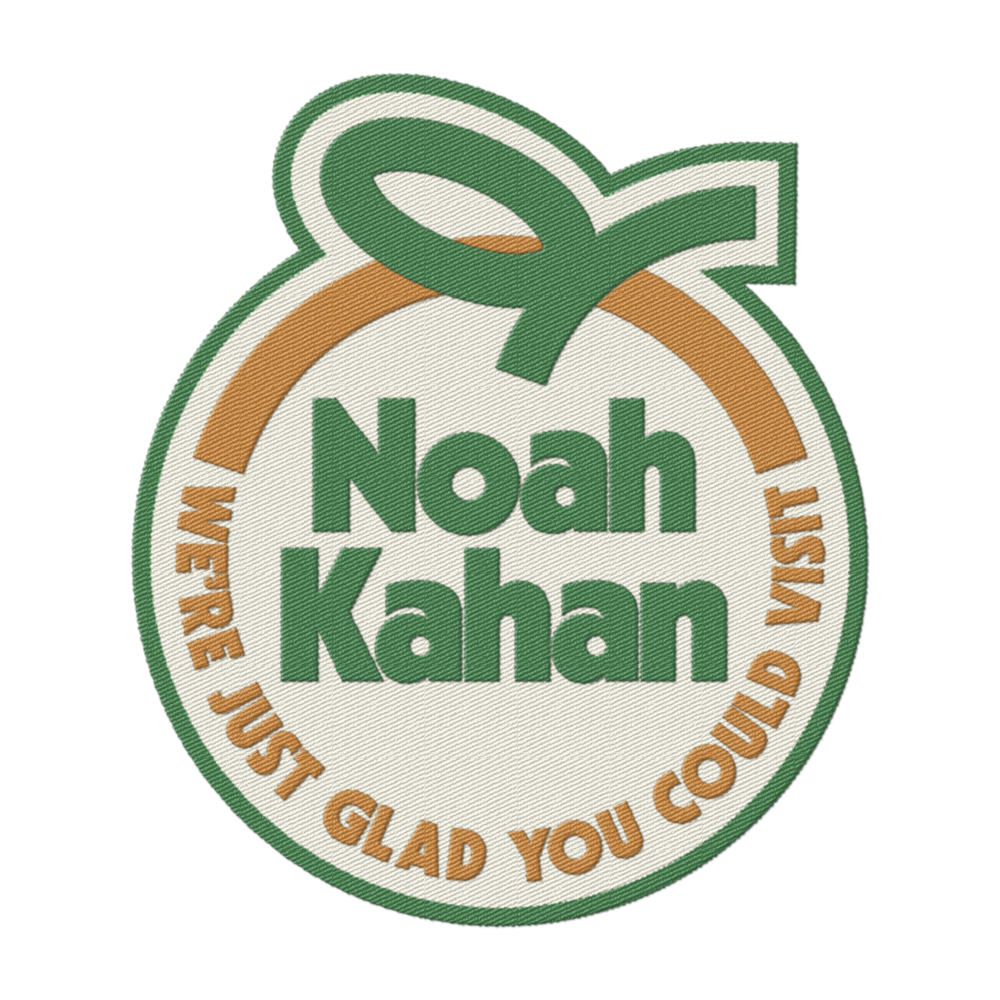 Noah Kahan orange juice embroidered iron on patch with "We're just glad you could visit" slogan in orange and green thread on a white background shaped to look like an orange with stem and leaf.